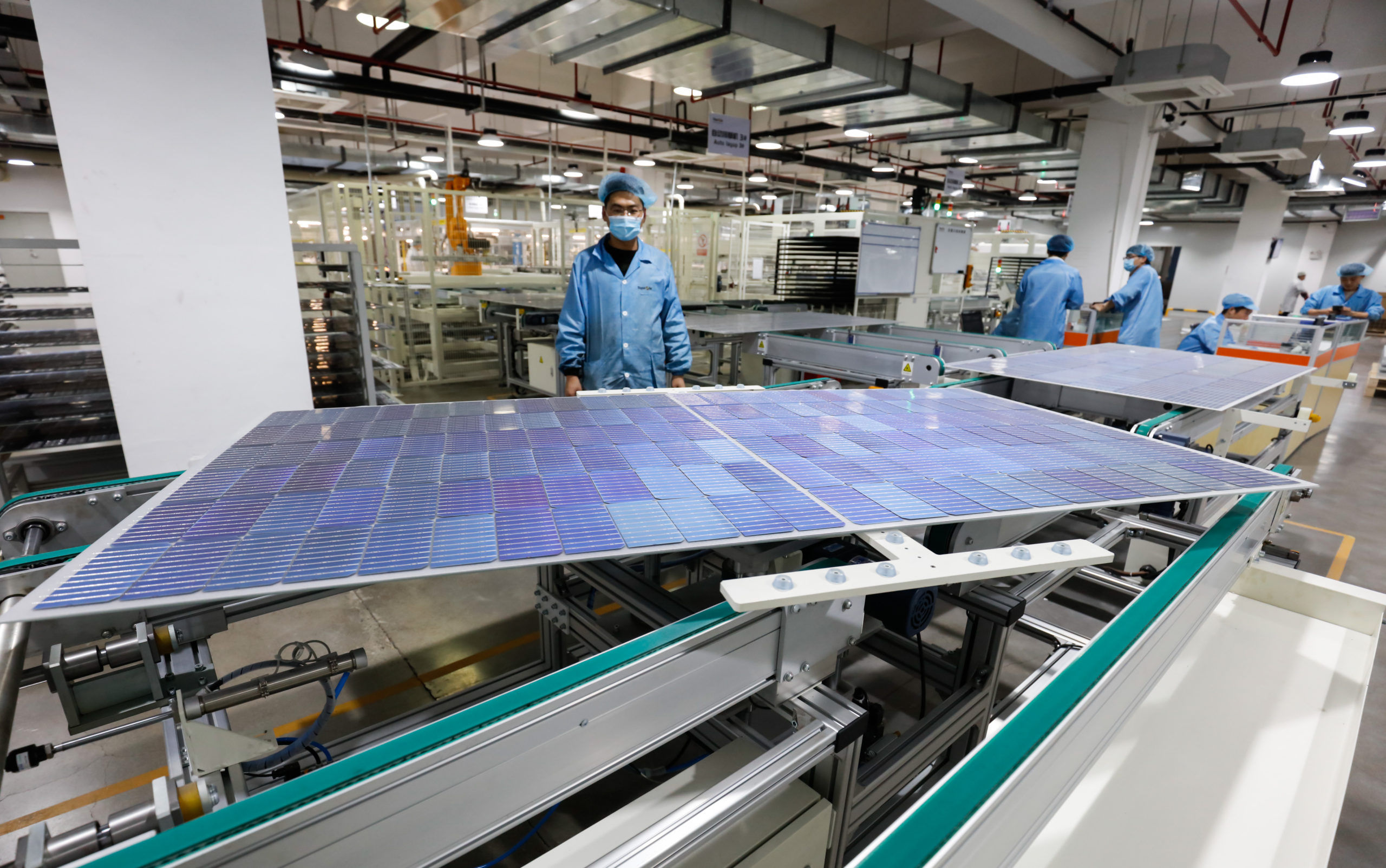 Workers operate equipment to produce photovoltaic circuit boards at a production workshop of a green energy technology company